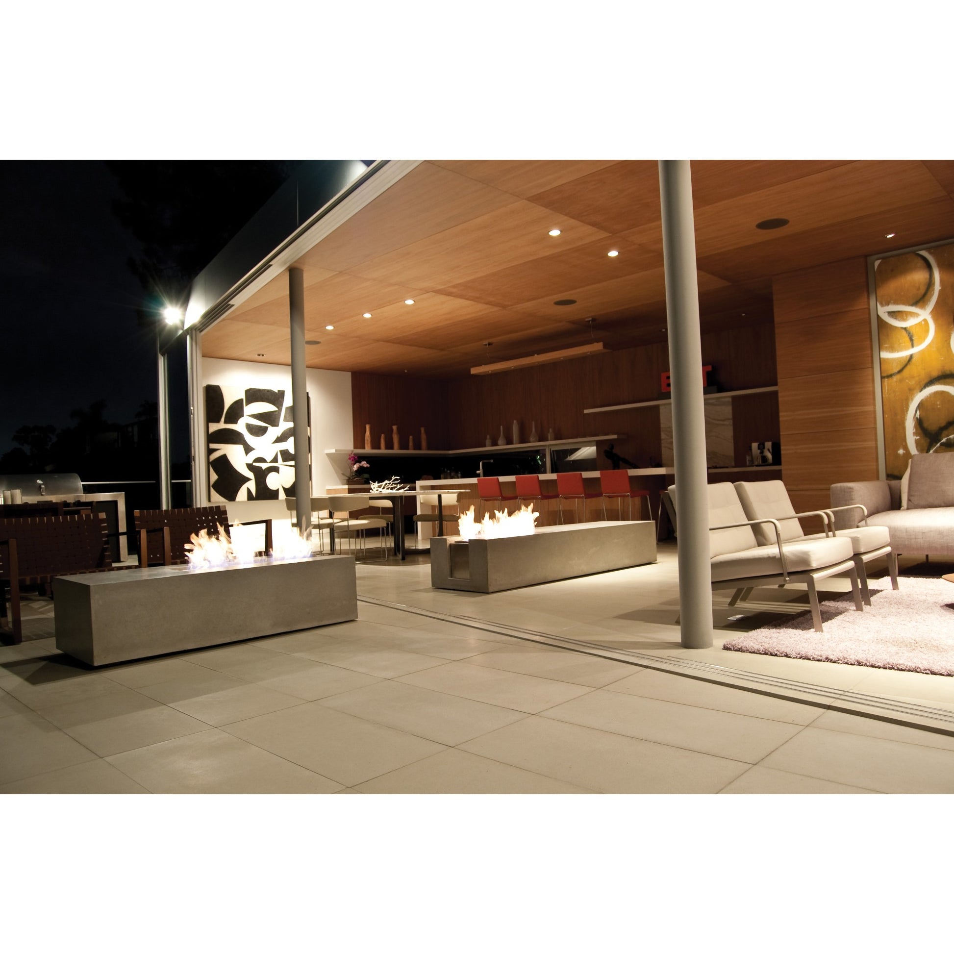 Modern outdoor patio with fire pits and seating area at night.