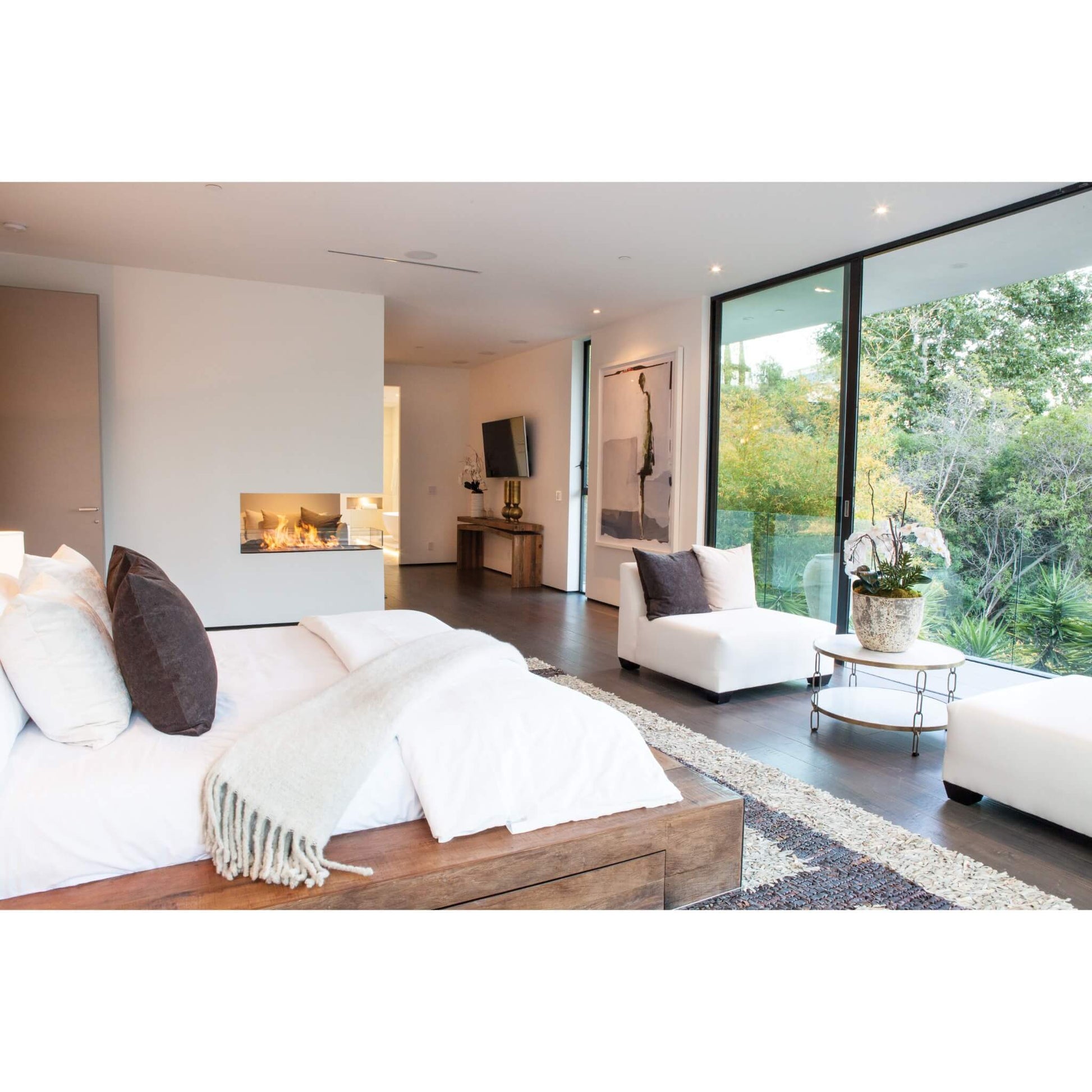 Modern bedroom with a bed, fireplace, and view of greenery outside.