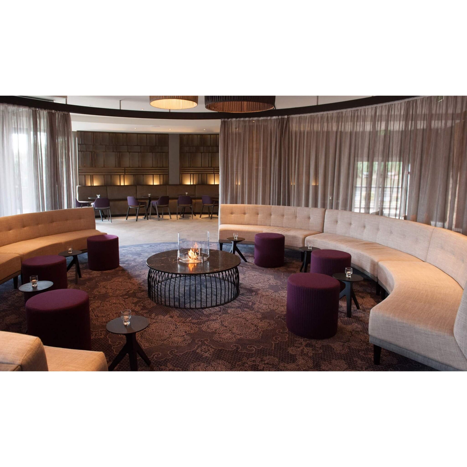 Modern lounge area with curved beige sofas, purple ottomans, and a fire pit table.
