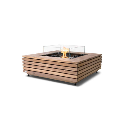 A black square concrete outdoor gas or bioethanol fire pit table with a visible fire in the center.