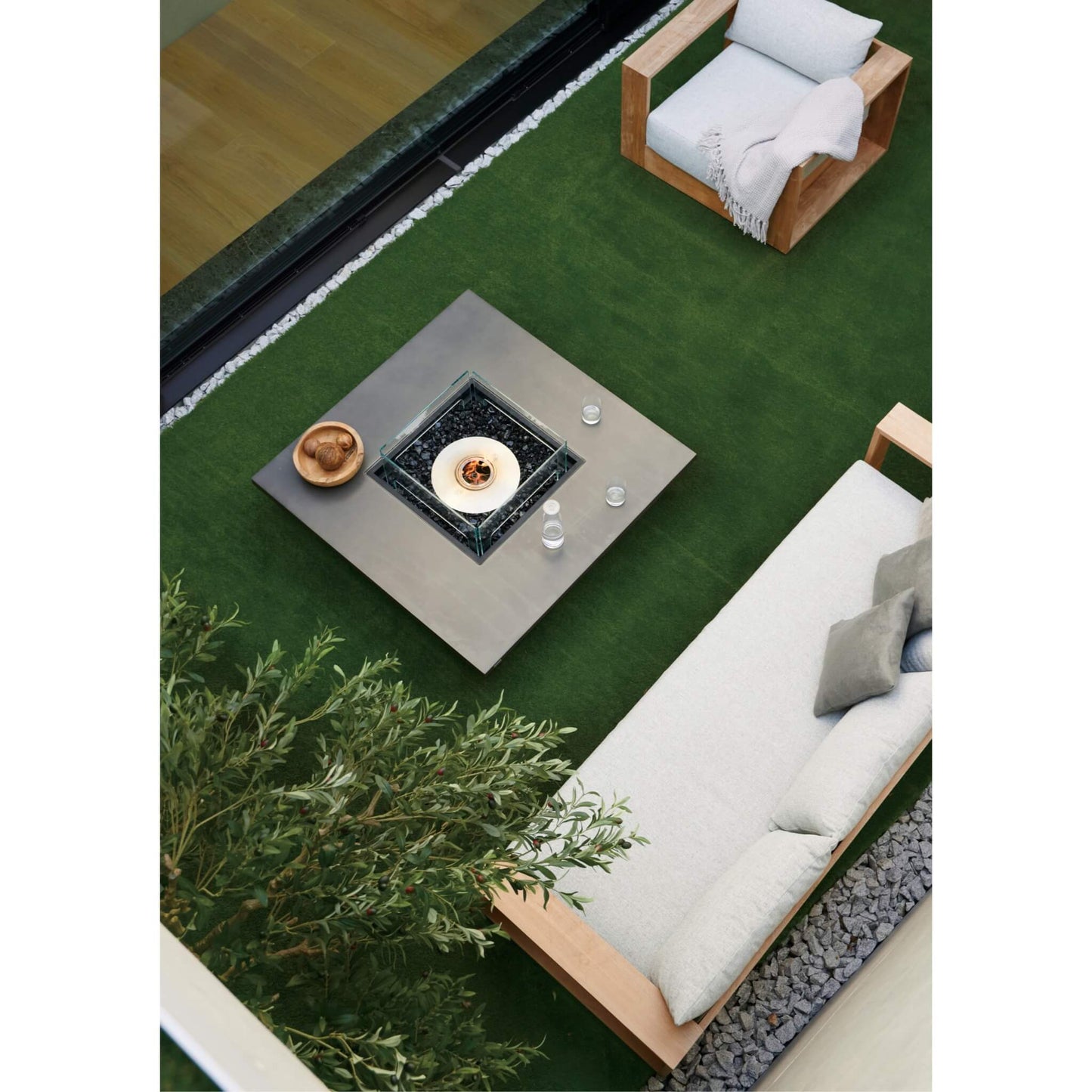 Outdoor setting with a fire pit table, chairs, and a sofa on a grassy area.