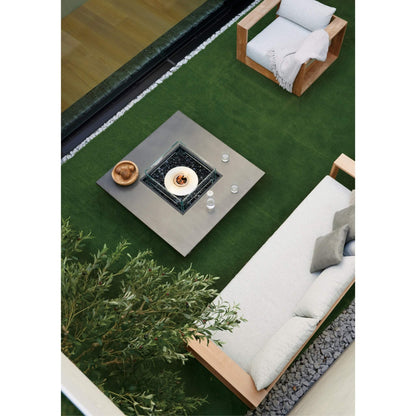 Outdoor setting with a fire pit table, chairs, and a sofa on a grassy area.