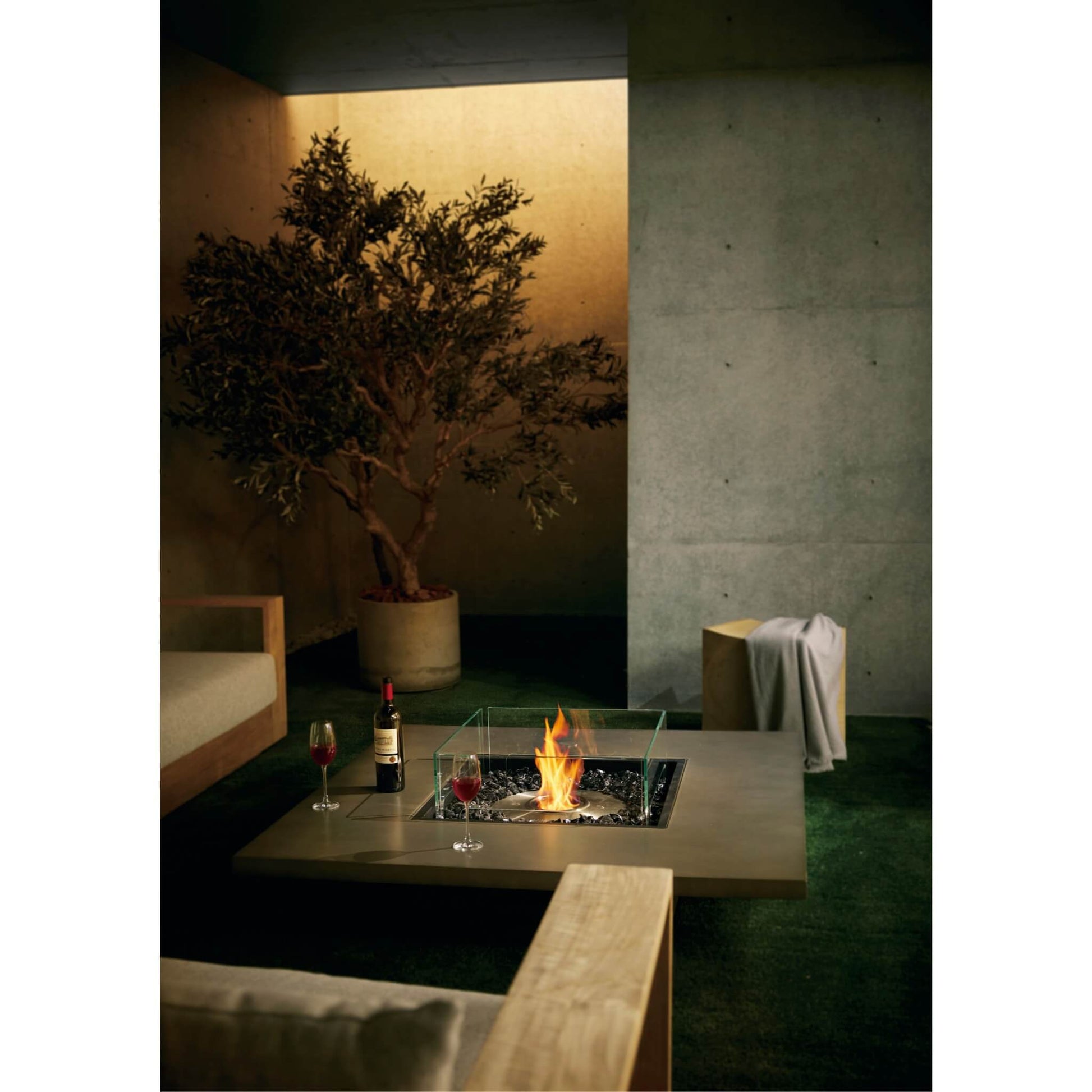 Modern outdoor setting with a fire pit, plant, and drinks on a patio.