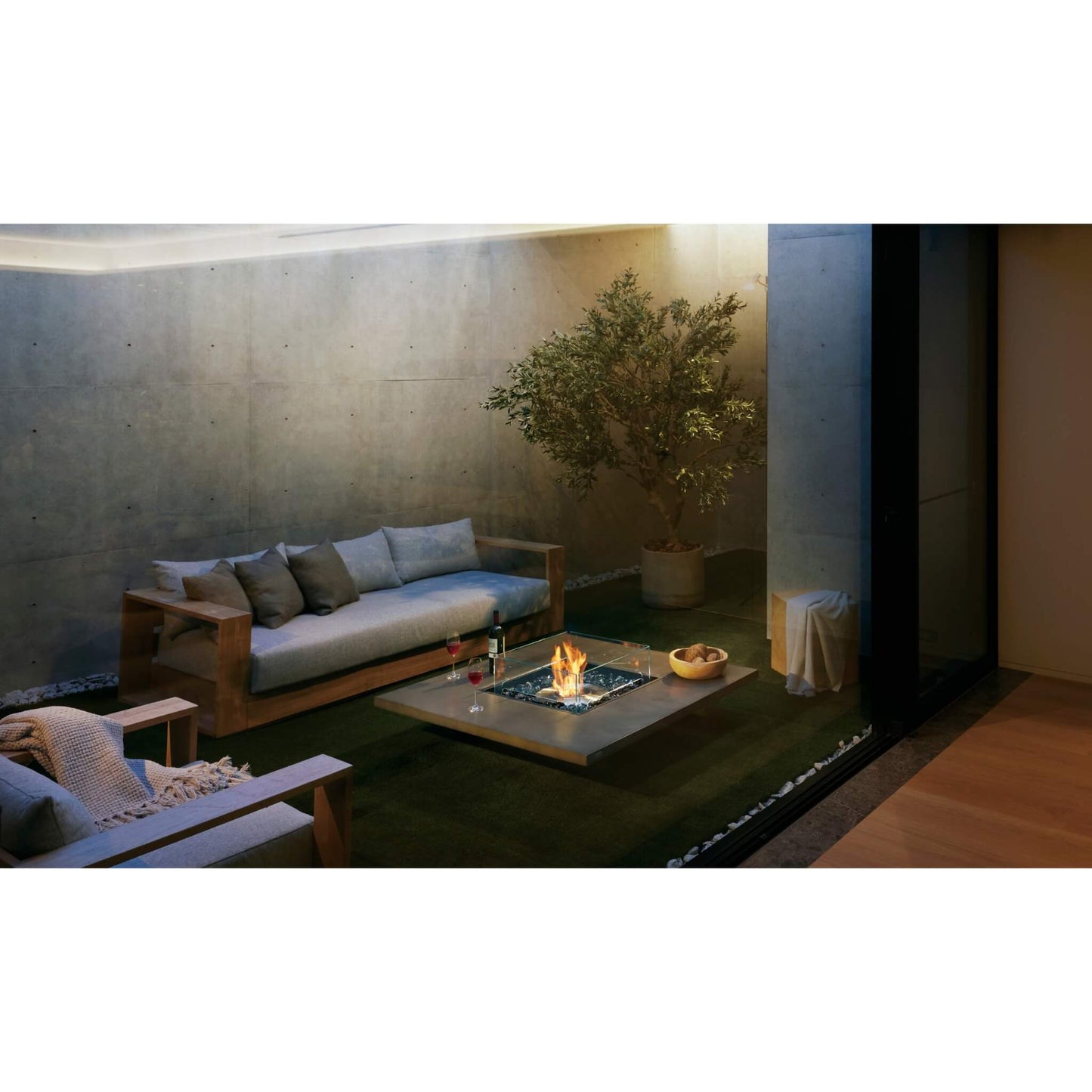 Modern outdoor living space with a fire pit, sofa, and potted plant.