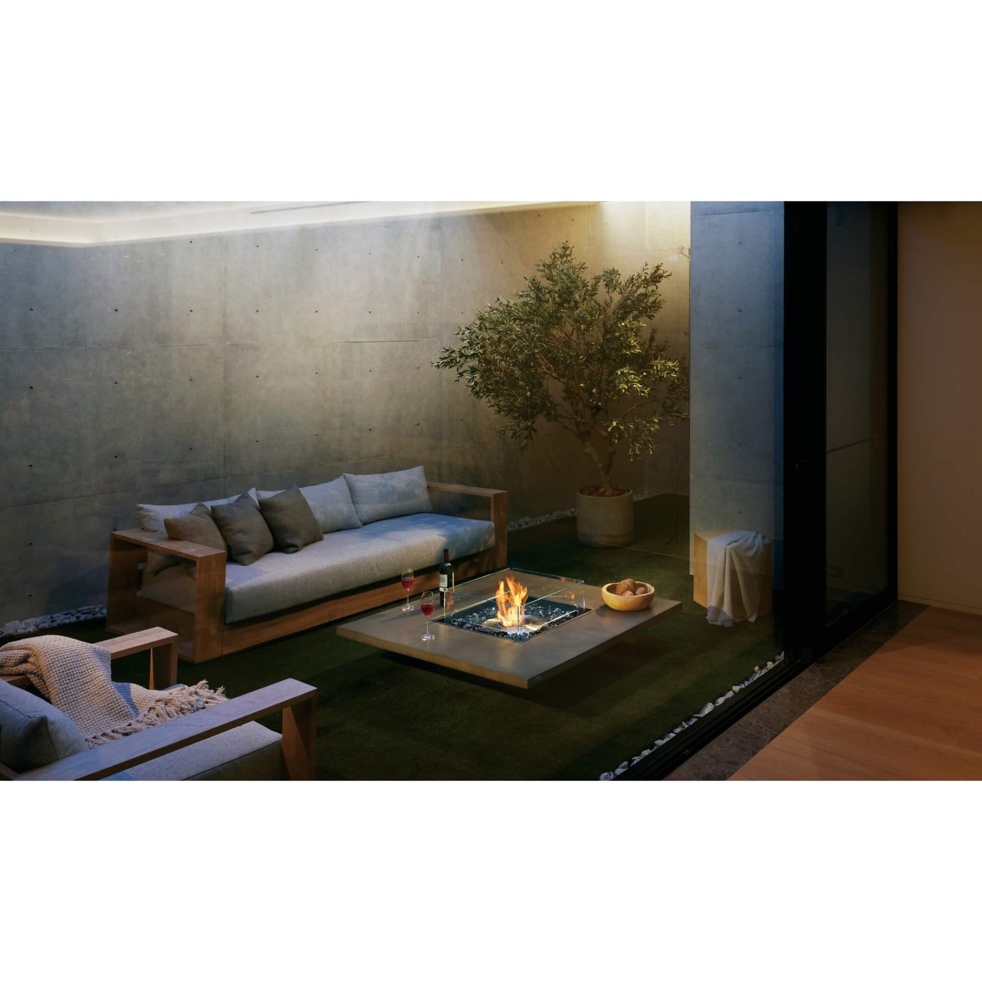 Modern outdoor living space with a fire pit, sofa, and potted plant.